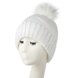 Close-up of white knit beanie featuring colorful sequin trim and a faux fur pom-pom