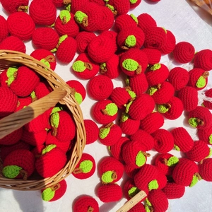 Close-up of handmade crochet red apples with green leaves and a scale ruler for size