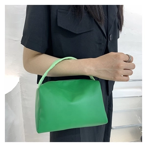 Close-up of green minimalist square handbag held by a model in a black shirt