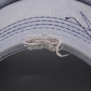 Macro detail of distressed light blue denim baseball cap brim with vintage stitching