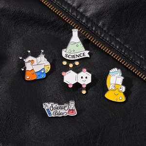 Macro detail of science theme enamel pins on black leather featuring lab flasks and beakers