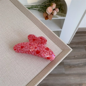 Close-up of pink medium hair claw clip with printed red hearts on a tray