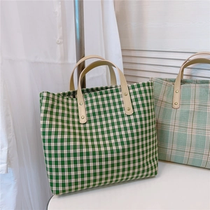 Detail of green plaid canvas tote bag featuring beige leather handle with metal rivets