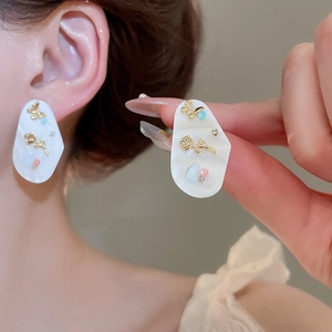 Détail de boucles d'oreilles fleur en nacre avec relief papillon doré et rose sur mannequin