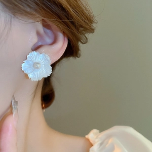 Close-up of elegant shell flower stud earring with pearl center on model ear