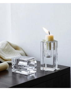 Detail of minimalist clear glass column candle holder with melted wax on wood surface