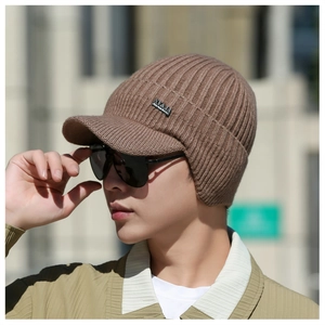 Dettaglio del cappello in maglia marrone con paraorecchie e logo metallico su uomo