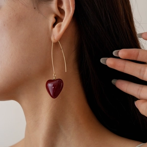 Detail shot of a long golden hook earring featuring a vibrant red heart-shaped pendant