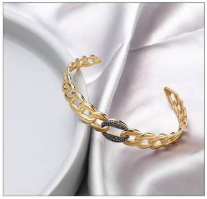 Close-up of gold C-shape open bangle with black zircon inlay on elegant silk background