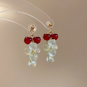 Macro detail of grape-shaped tassel earrings featuring resin cat-eye beads and gold hooks