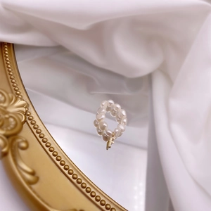Detail of freshwater pearl ring with a golden letter F charm on a reflective mirror surface
