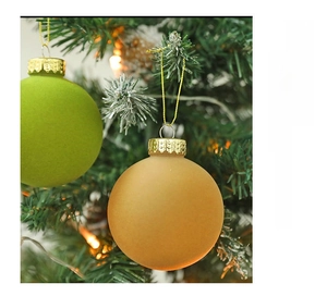 Close-up of green and orange velvet Christmas balls hanging on snow-dusted tree branches
