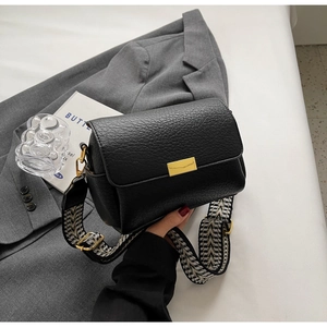 Détail d'un sac bandoulière noir en cuir grainé avec sangle géométrique et fermoir doré