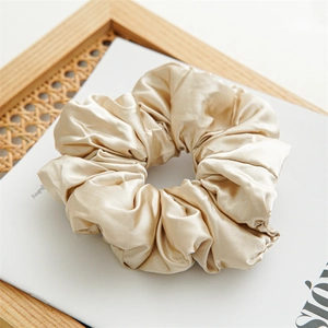 Macro shot of champagne gold satin scrunchie with silky folds and textured sheen