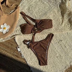Coffee brown bikini set with asymmetric cutouts and metallic ring details on flat lay