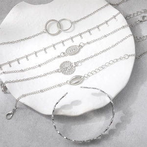Close-up of silver bracelet set with shell and coin charms on white ceramic tray