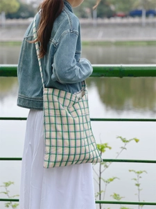Outdoor shot of a plaid cotton tote bag with green and lilac checks on a model's shoulder