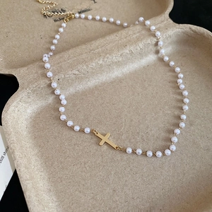 Detailed close-up of a pearl necklace with a central gold cross pendant on beige paper
