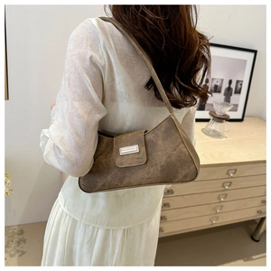 Brown faux suede underarm bag with metal buckle shown on model in minimalist interior