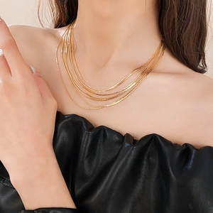 Detail of layered gold-plated snake bone necklace on model with black outfit