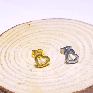 Detailed view of minimalist heart stud earrings in gold and silver on wooden stand