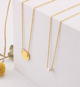 Detail of layered gold stainless steel necklaces with round disk and pearl pendants