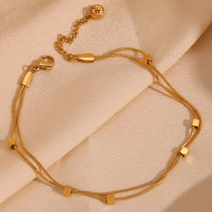 Detail of 18K gold-plated double-layer snake chain anklet with cube pendants on silk fabric
