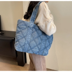 Détail d'un sac cabas en denim bleu matelassé avec surpiqûres en losanges sur un mannequin