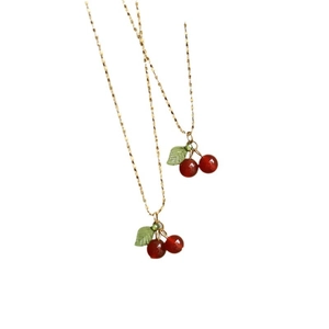 Elegant gold chain necklaces with red cherry pendants and green leaves on white background