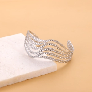 Detail of silver wave-patterned hollow cuff bangle on a textured stone display