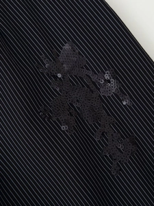 Détail macro d'une broderie de fleurs à paillettes sur un tissu de costume rayé