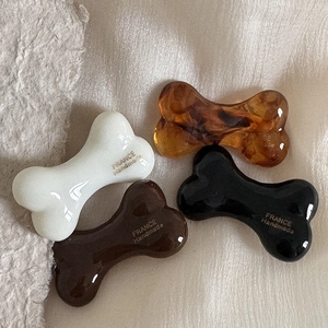 Set of bone-shaped hair clips in white, amber, and brown acetate with gold lettering