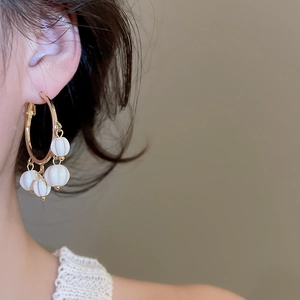 Close-up of golden hoop earrings with white pumpkin-shaped ribbed beads on a model