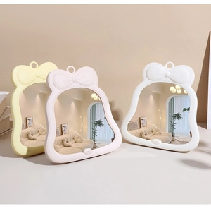 Trois miroirs de maquillage avec nœud papillon en jaune, rose et blanc posés sur une table