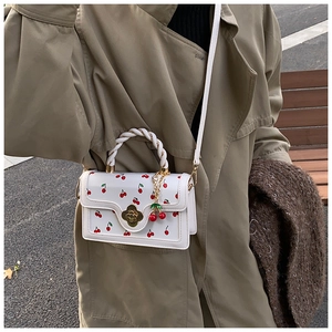 Close-up of white leather handbag with red cherry print and golden flower buckle
