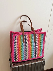 Rainbow striped woven tote bag with brown leather handles on a silver suitcase