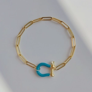 Golden paperclip chain bracelet featuring a vibrant blue horseshoe U-shaped clasp