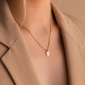 Golden box chain necklace with square letter R pendant worn by model in a beige suit