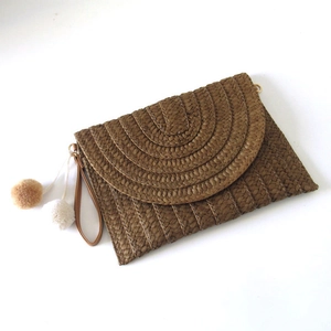 Detailed top view of a dark brown paper straw woven clutch with decorative pom poms