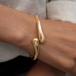 Macro shot of minimalist gold teardrop open cuff bracelet with a polished metal finish