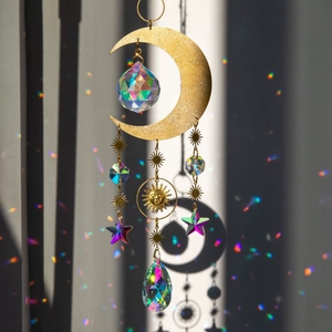 Brass moon and star crystal suncatcher casting rainbow light on a neutral background
