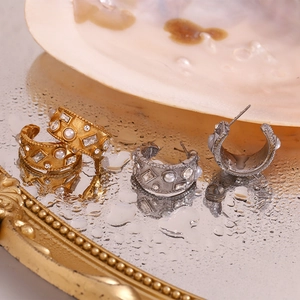 Detail of C-shaped gold and silver hoop earrings with pearls and zircons on a wet mirror