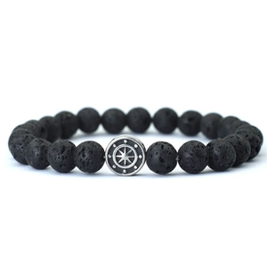 Macro detail of black volcanic stone bracelet with silver compass charm and porous texture