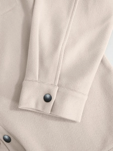Detail of light beige wool jacket cuff with neat stitching and dark button closure