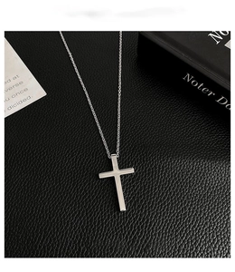 Detailed close-up of a silver titanium steel cross pendant on black textured leather