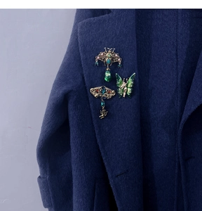 Detail of vintage emerald style insect brooches on dark navy wool coat with gold filigree