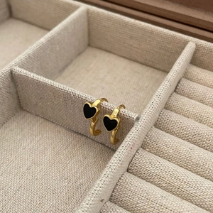 Minimalist heart-shaped gold-framed black drop earrings hanging on a linen jewelry box