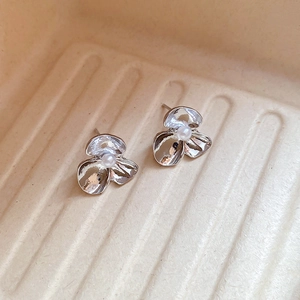 Detail of silver floral stud earrings with centered white pearl on beige textured surface