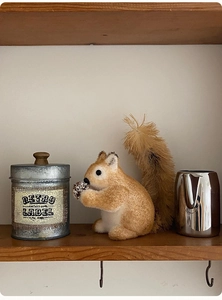 Close-up of a realistic plush squirrel with pine cone on a rustic wooden shelf