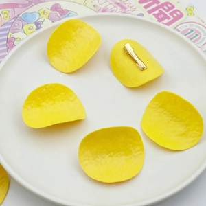 Five yellow potato chip hair clips on a white ceramic plate with golden alligator clips